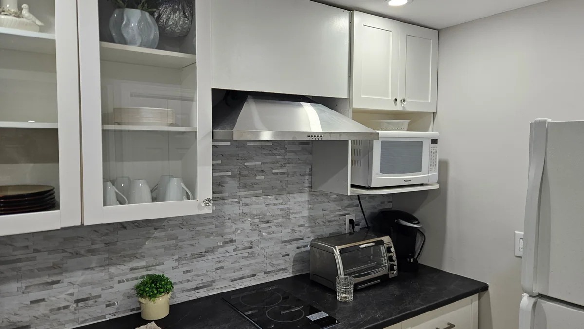 Compact basement kitchenette with white cabinetry and mosaic backsplash