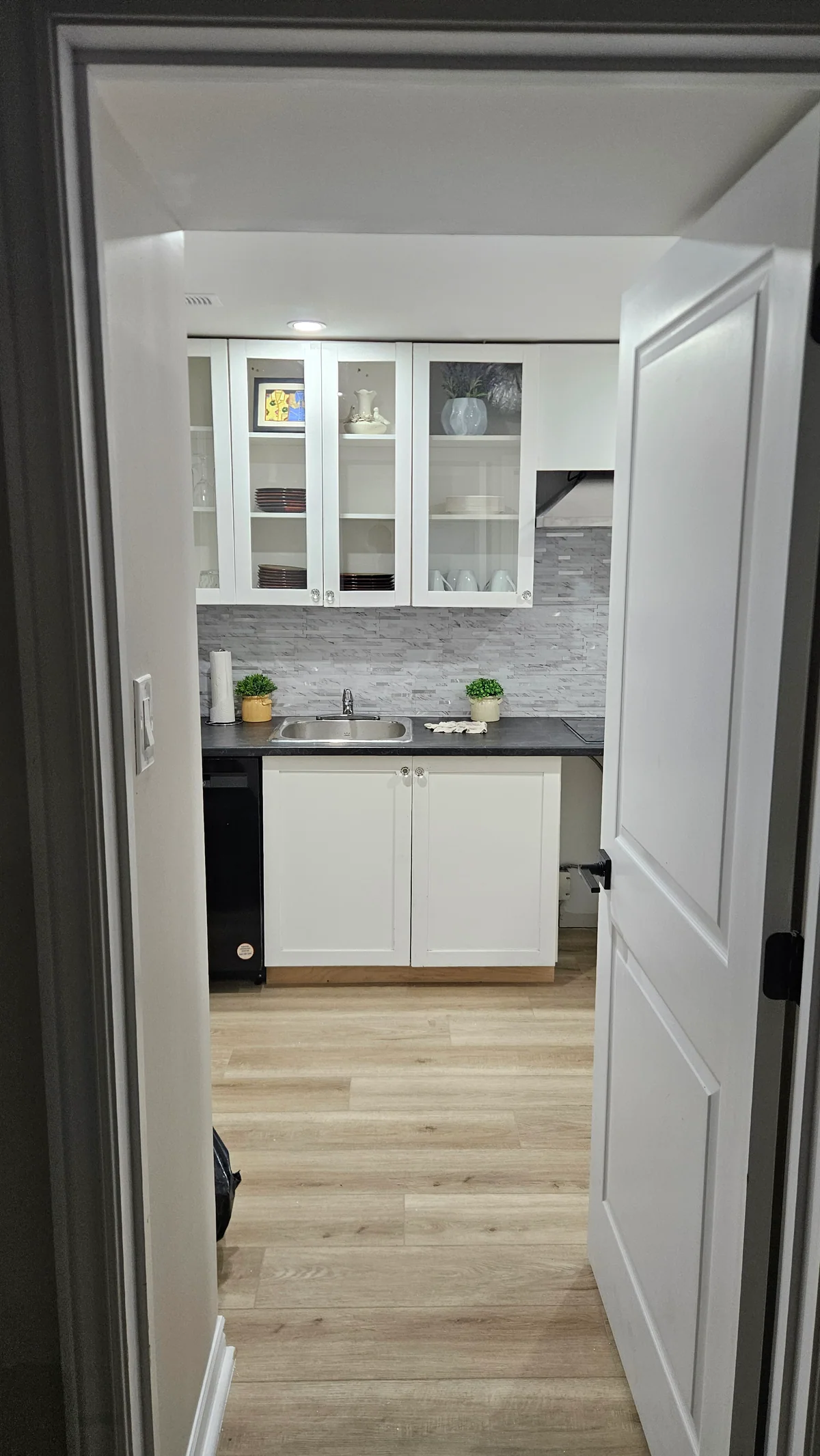 Doorway view into a completed basement kitchenette with white cabinetry
