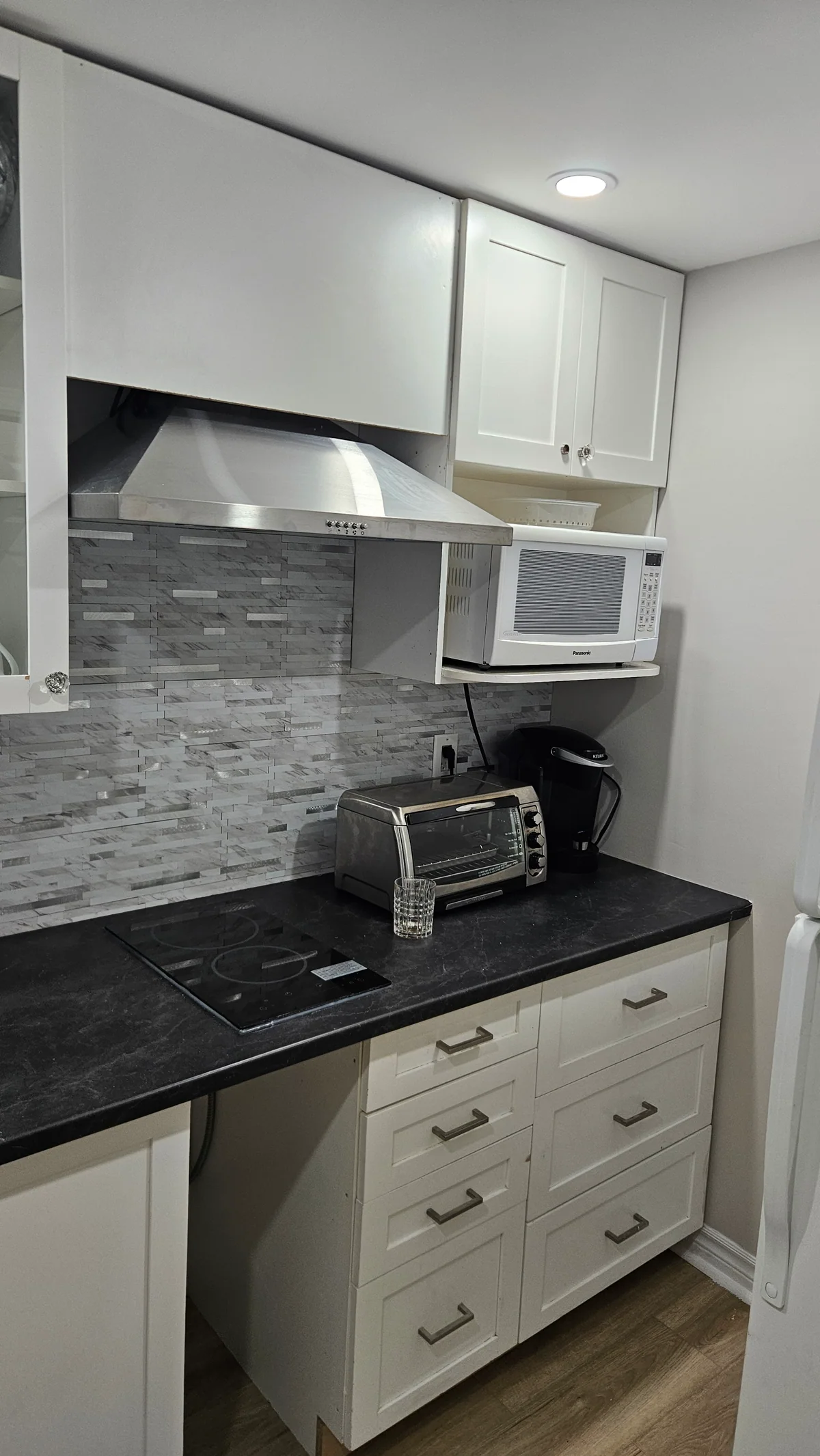 Compact basement kitchenette with white cabinets and stainless range hood