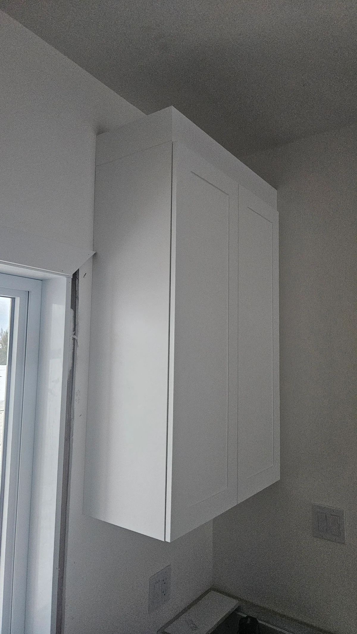 Tall white corner cabinets fitted beside a bright window
